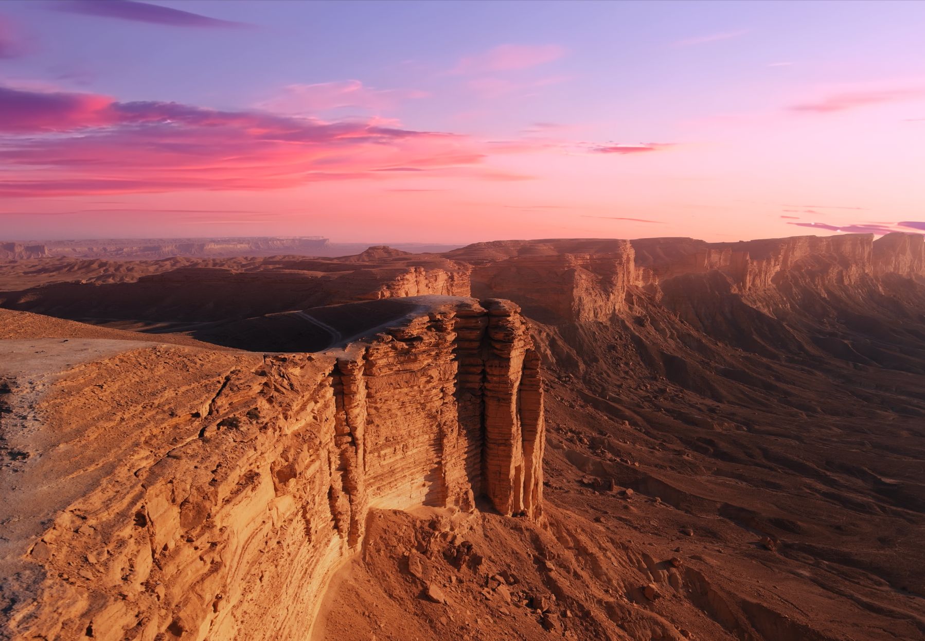 The Edge of the World cliffs near Riyadh at sunset under a pink and violet sky